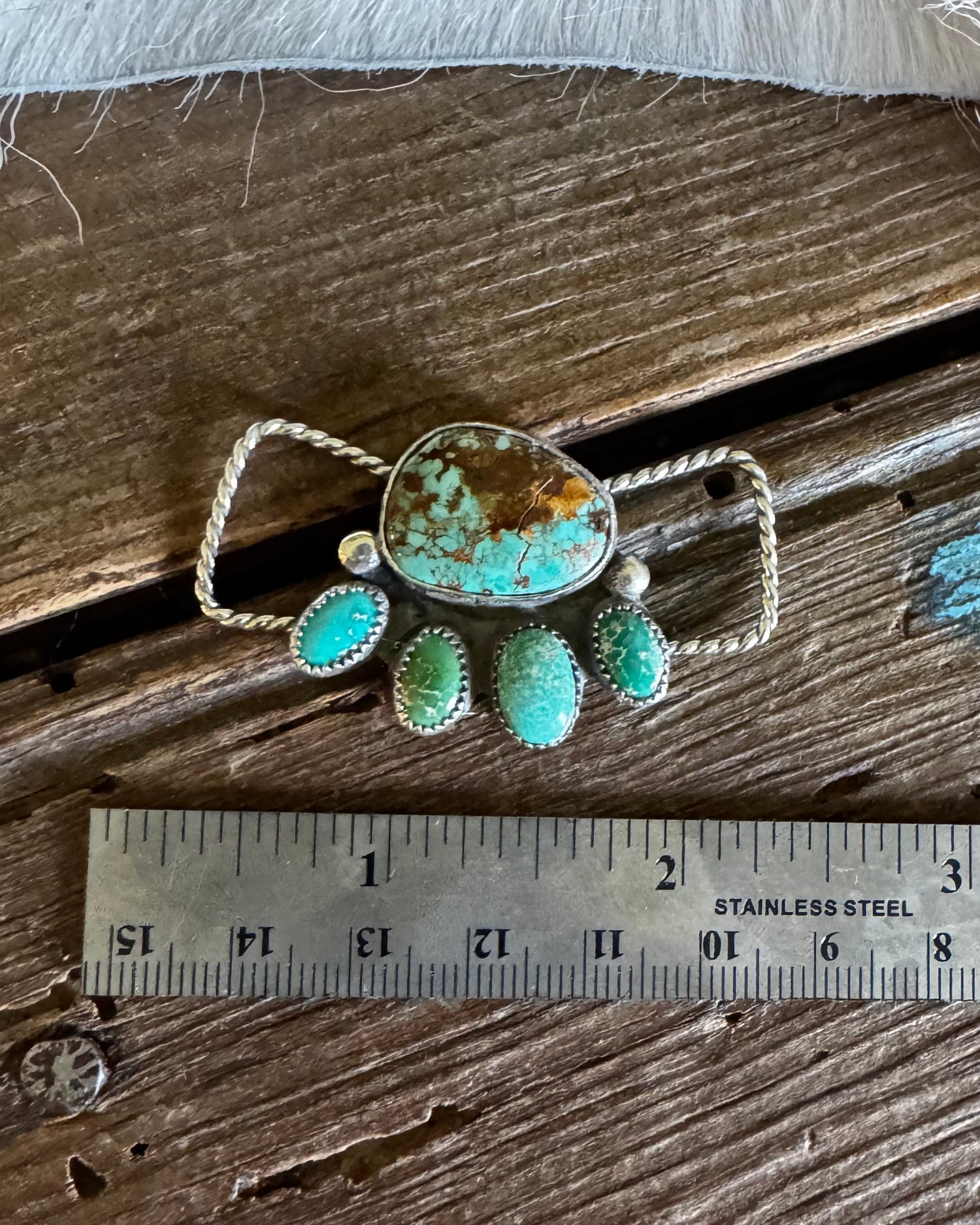 Turquoise and silver twilly slide on a wooden surface with a ruler for scale.
