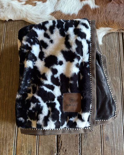cow print blanket with ribbon trim on a wooden surface