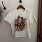 White t-shirt with a graphic design of a horse and text, hanging on a wooden hanger against a white wall.