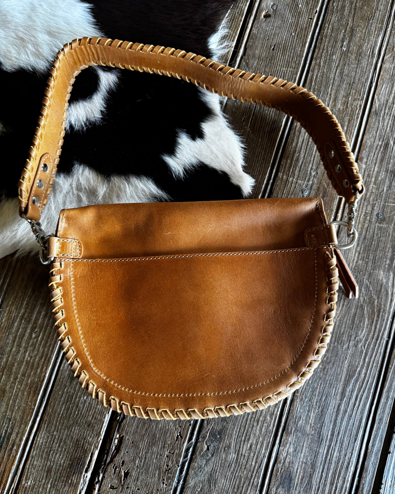 Brown leather handbag on a wooden surface with cowhide rug