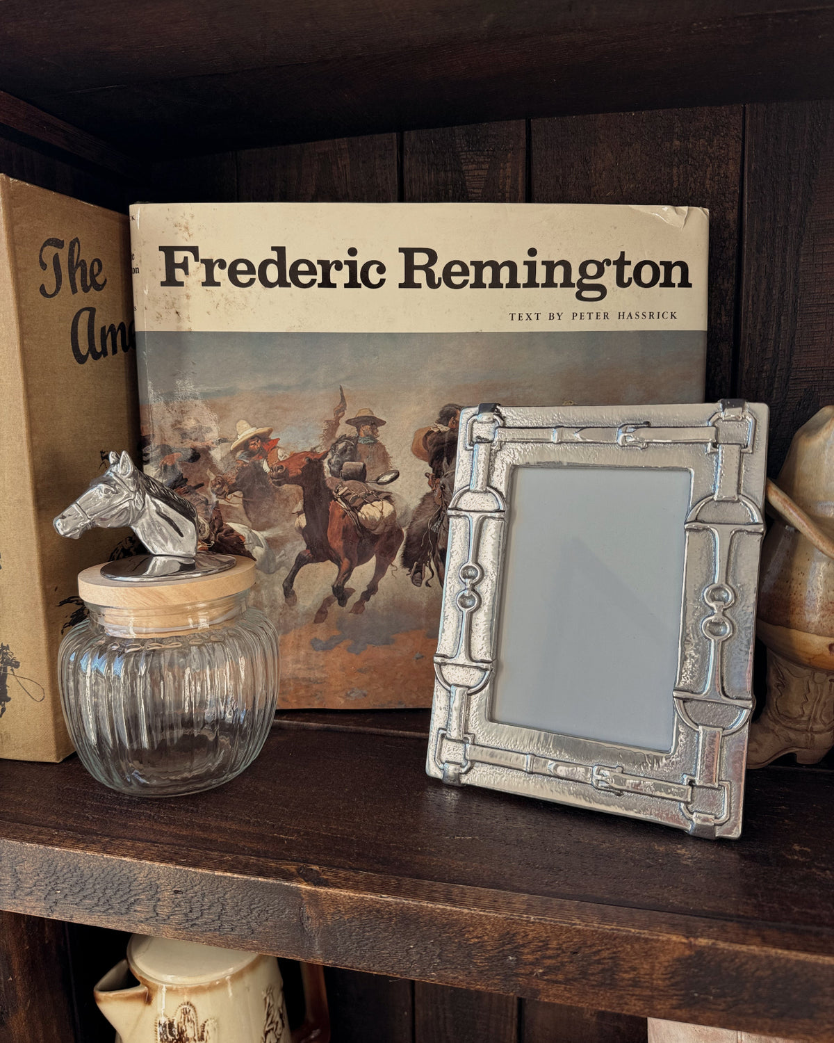 Decorative items on a wooden shelf including a book titled 'Frederic Remington', a picture frame, and a glass jar.