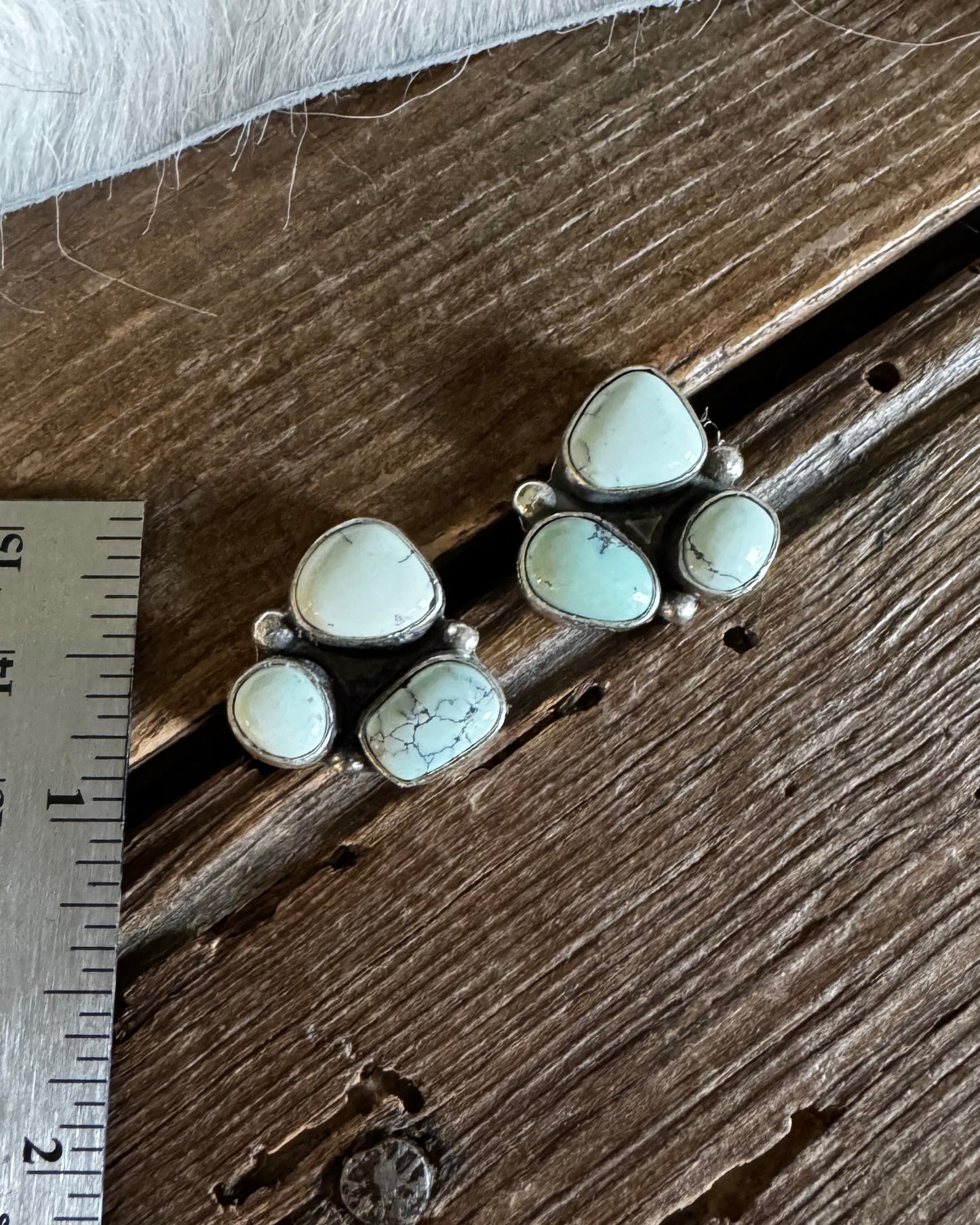 Jewelry with white stones on a wooden surface next to a ruler for scale.