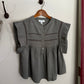 Green blouse with lace trim on a wooden hanger against a white wall.