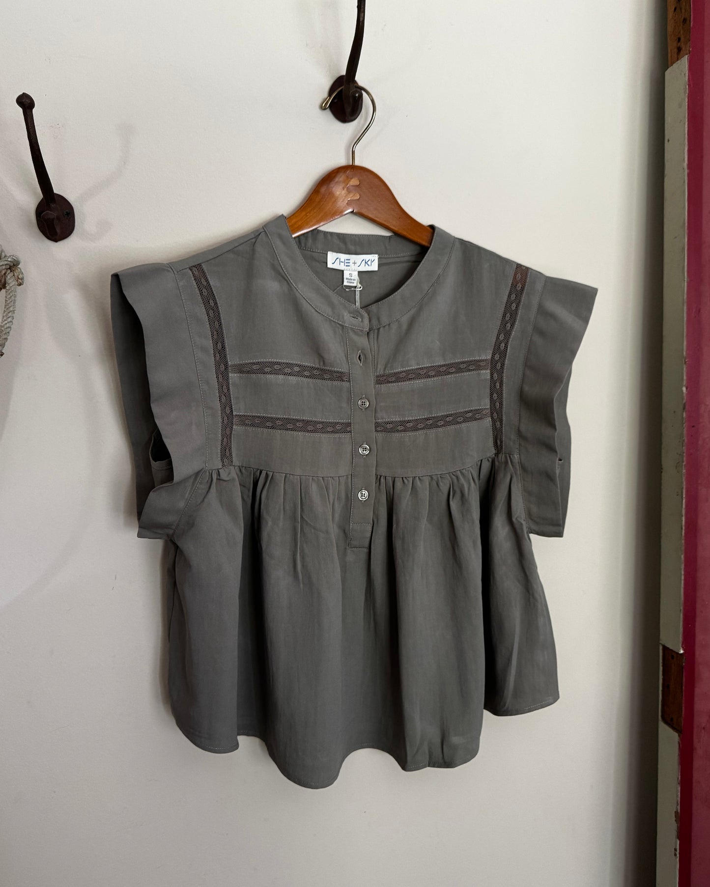 Green blouse with lace trim on a wooden hanger against a white wall.