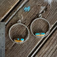 Pair of silver earrings with turquoise stones on a wooden surface with a ruler for scale.