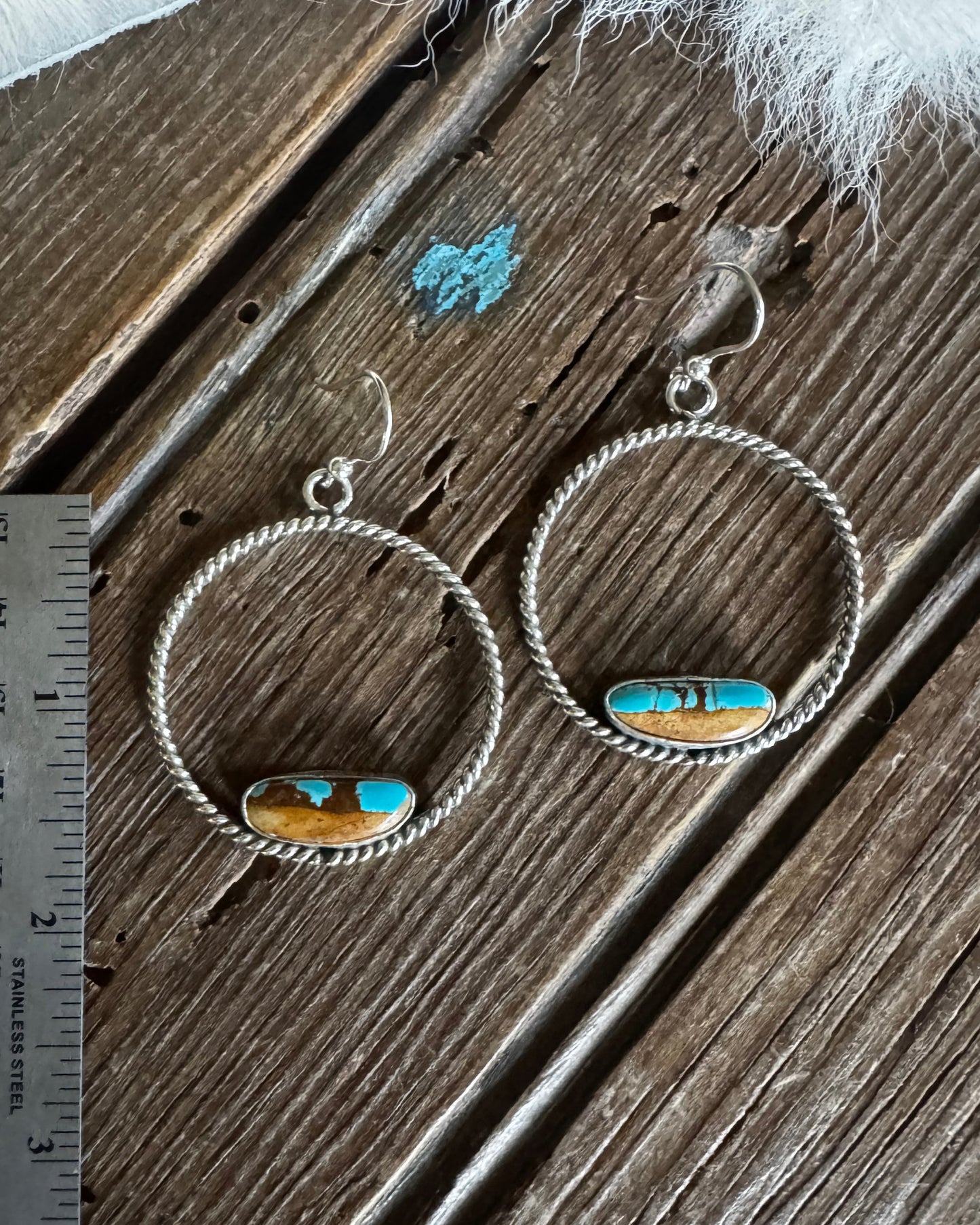 Pair of silver earrings with turquoise stones on a wooden surface with a ruler for scale.