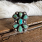 A sterling silver ring with a floral cluster of turquoise stones, displayed on a rustic wooden surface with a black and white cowhide rug behind it.