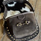 Brown leather bag with gold studs and a horse bit clasp on a wooden surface.