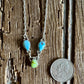 Necklace with turquoise and green beads on a wooden surface next to a quarter for scale.