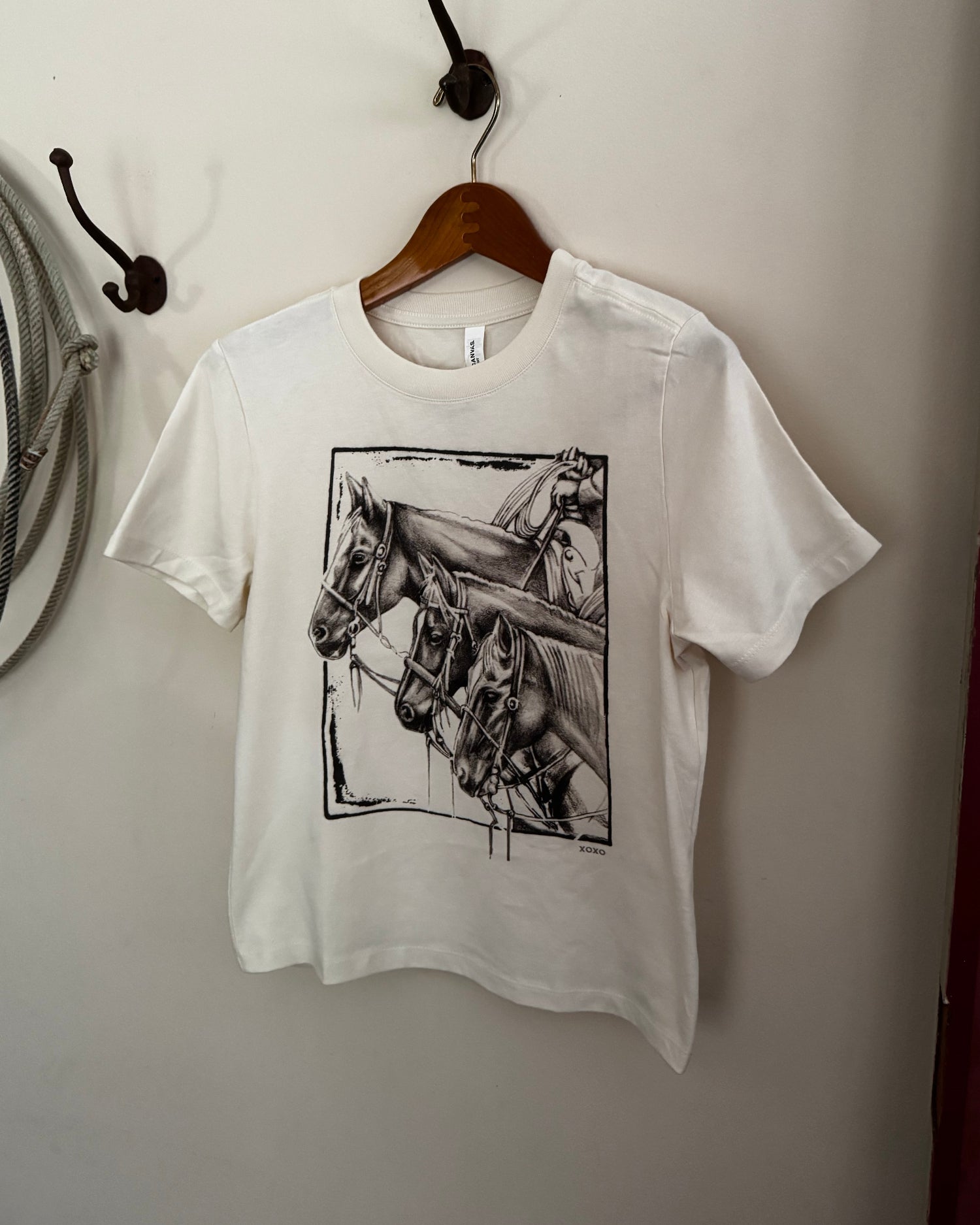 White t-shirt with horse graphic on a hanger against a white wall.