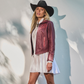 Woman wearing a burgundy leather jacket and white dress with a black cowboy hat against a light background