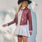 Woman wearing a red leather jacket, white dress, and black hat against a light background