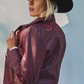 Woman wearing a burgundy leather jacket with red embroidery and a black cowboy hat against a light gray background