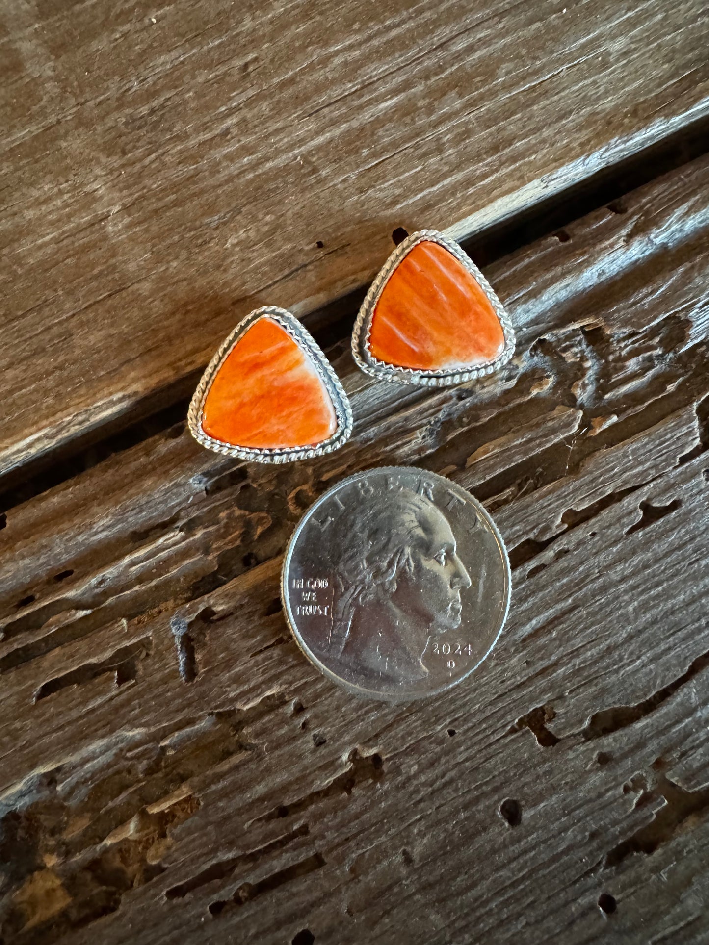Pair of orange triangular earrings next to a quarter on a wooden surface
