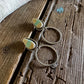 Pair of silver hoop earrings with green gemstones on a wooden surface.