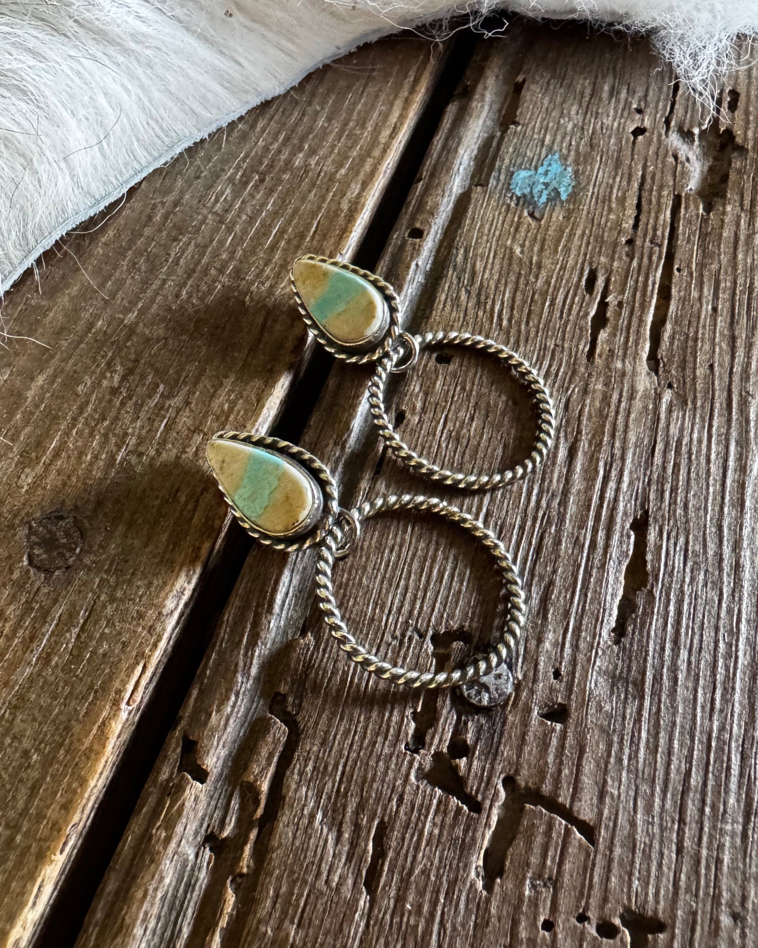 Pair of silver hoop earrings with green gemstones on a wooden surface.