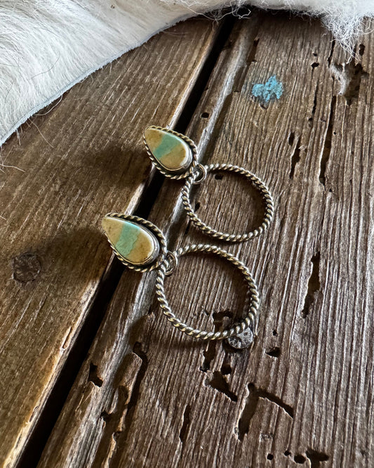 Pair of silver hoop earrings with green gemstones on a wooden surface.