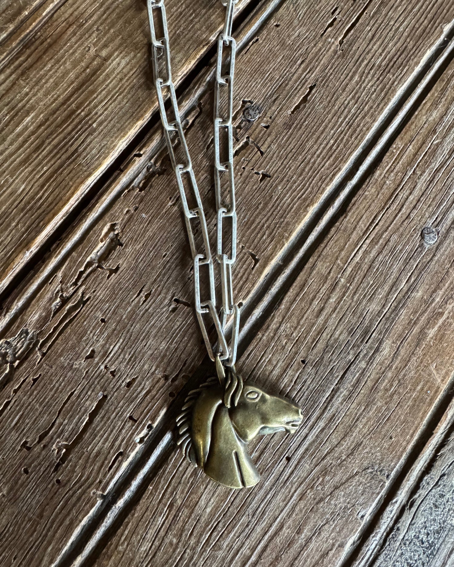 Brass horse head pendant necklace on rustic wood background