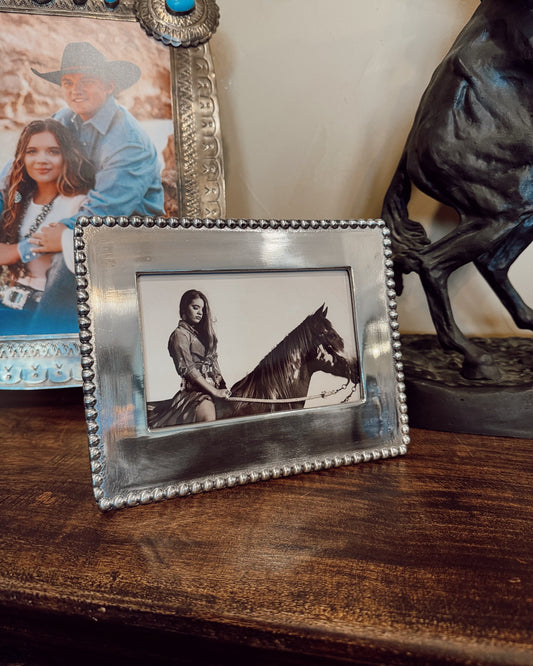 Decorative photo frame with a picture of a person on a horse inside, placed on a wooden surface.