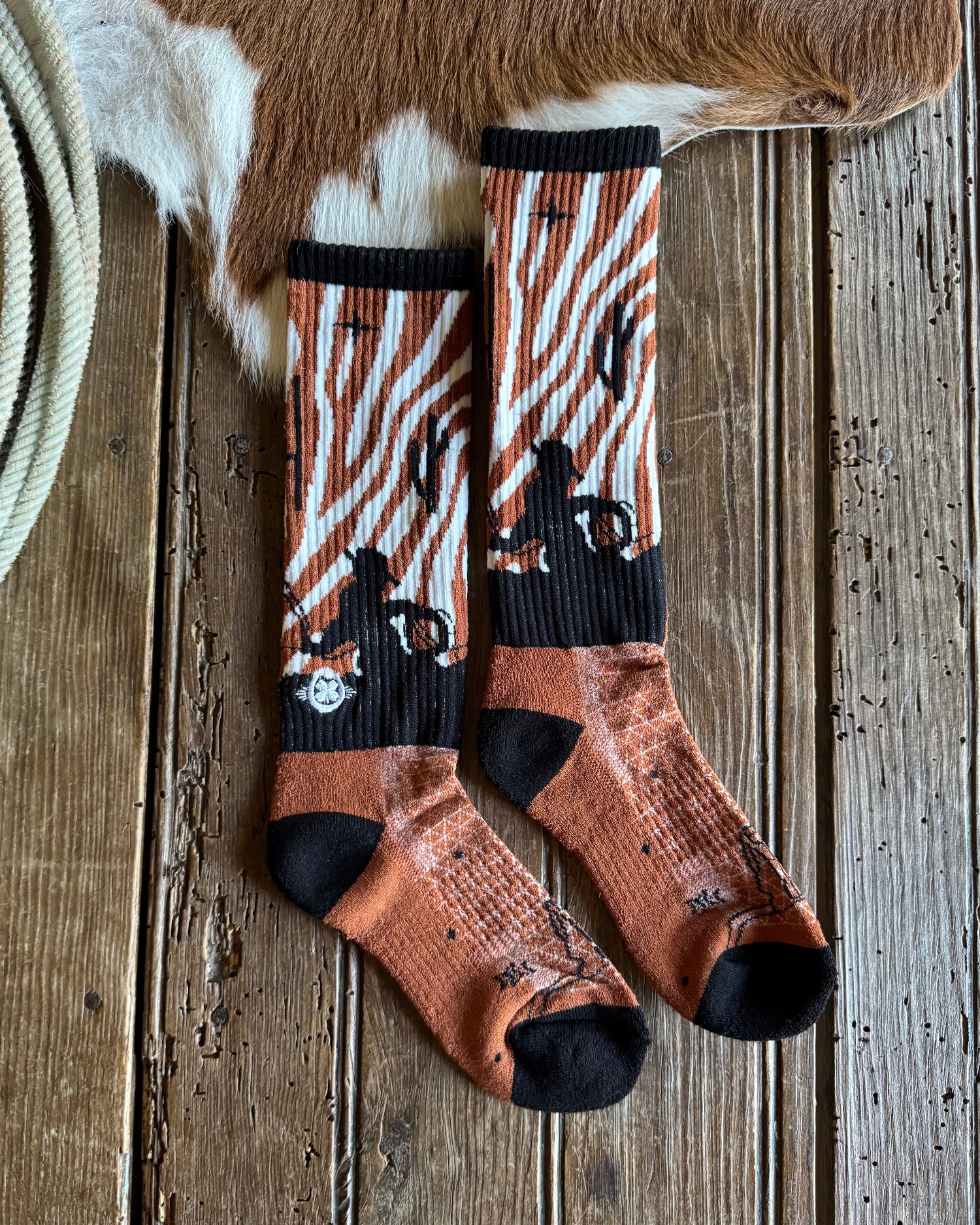 Pair of patterned socks on a wooden surface with a cowhide rug and rope.