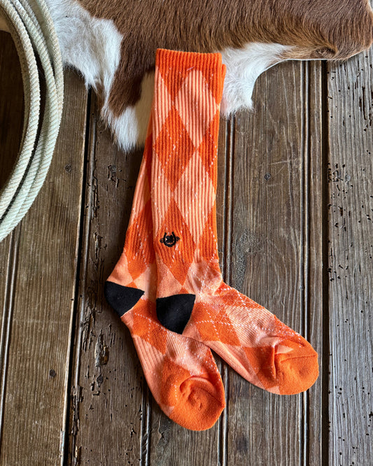 Orange socks on a wooden surface with a cow's hide in the corner