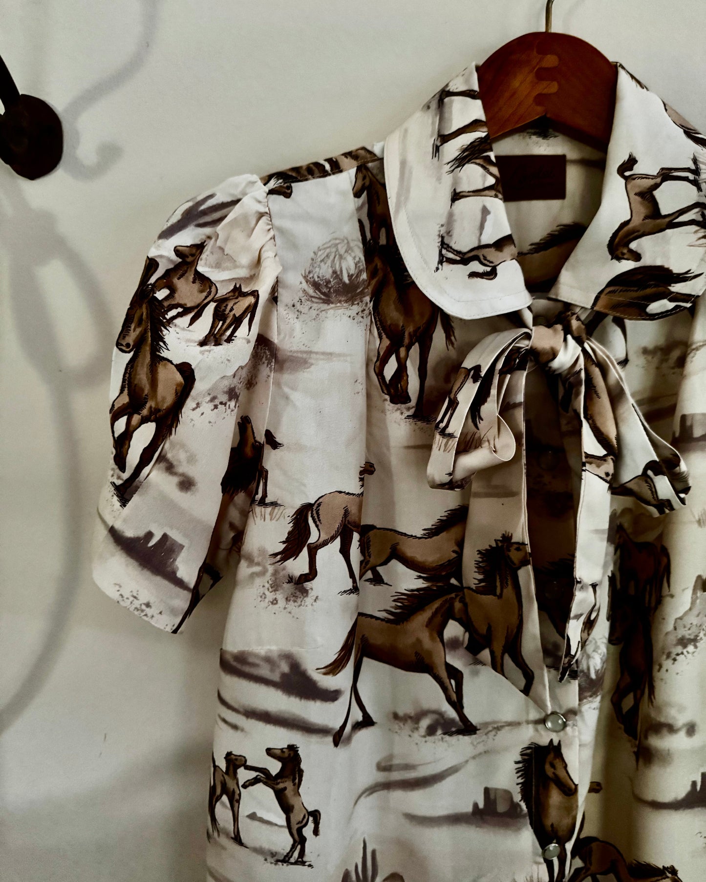 Shirt with horse pattern on a hanger against a plain background