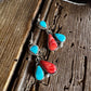 Pair of earrings with turquoise and red stones on a wooden surface