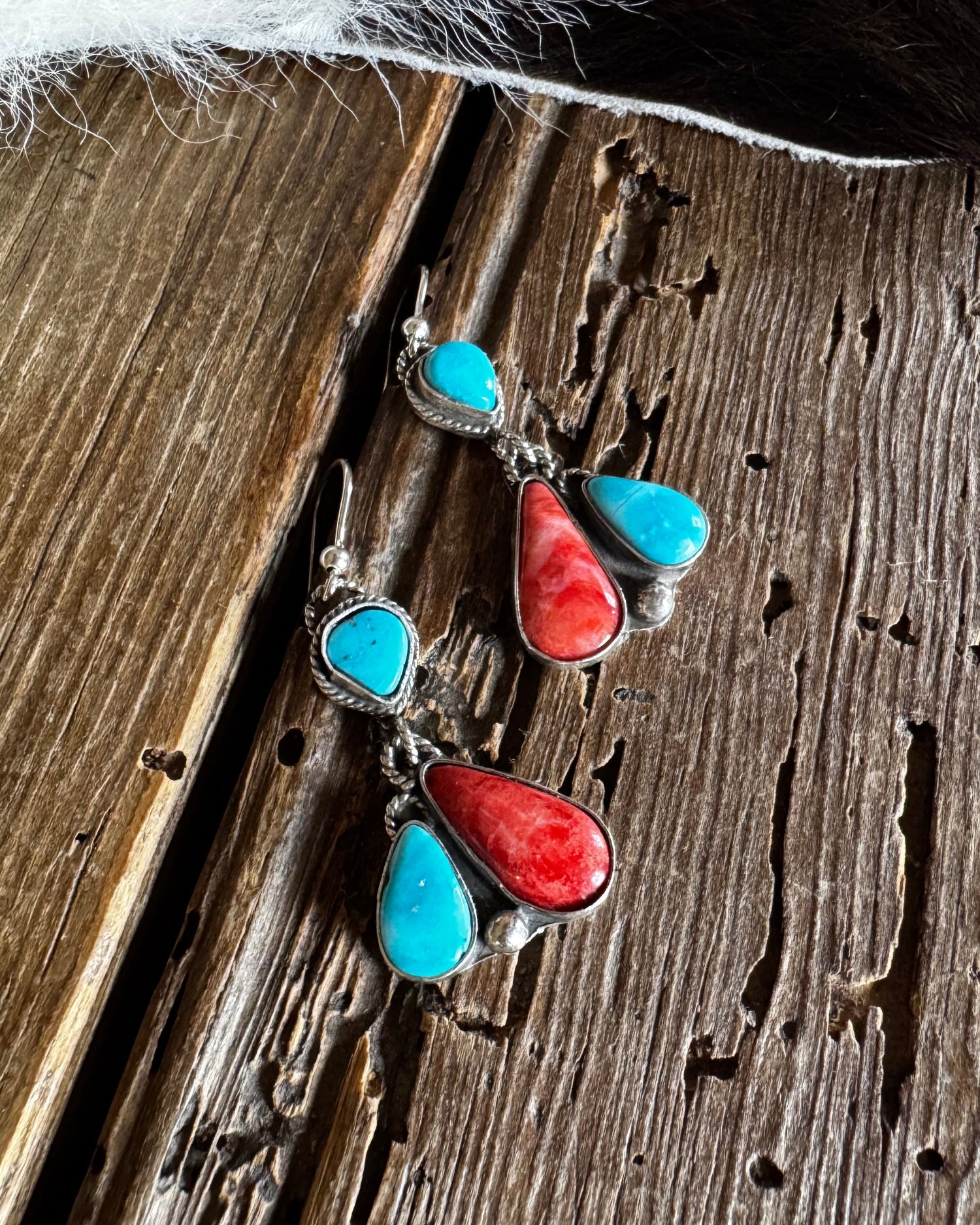 Pair of earrings with turquoise and red stones on a wooden surface