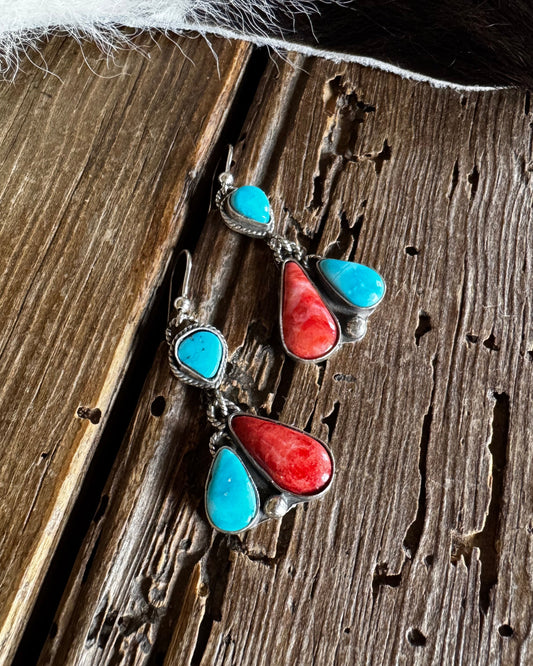 Pair of earrings with turquoise and red stones on a wooden surface