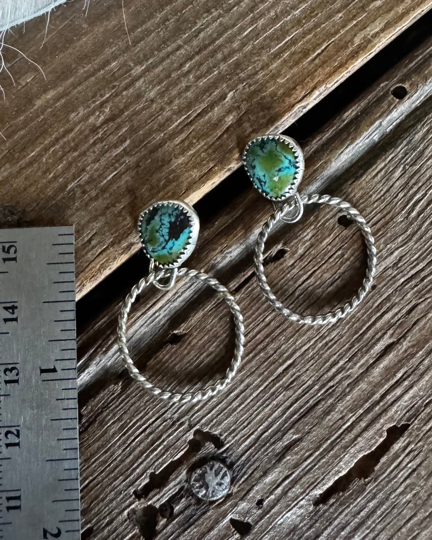 Silver hoop earrings with turquoise stones on a wooden surface next to a ruler.