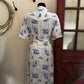 White dress with blue patterns on a mannequin against a neutral wall.