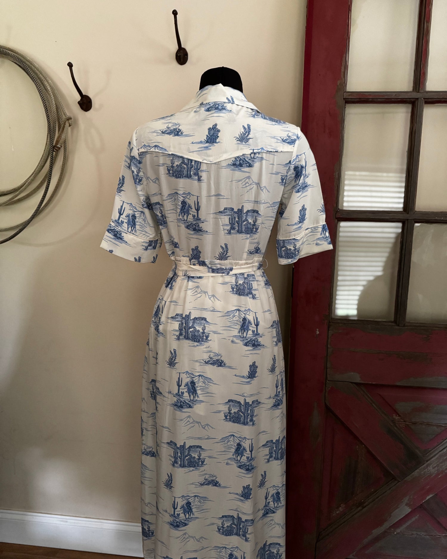 White dress with blue patterns on a mannequin against a neutral wall.