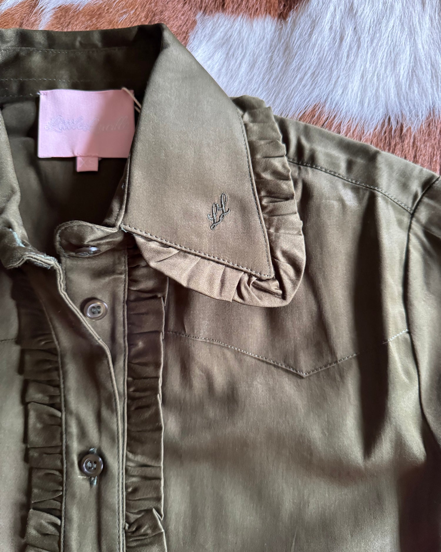 Olive green blouse with a brand logo on a textured surface