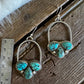 A pair of silver hoop earrings with heart-shaped clusters of turquoise stones, displayed on a rustic wooden surface next to a metal ruler for scale.