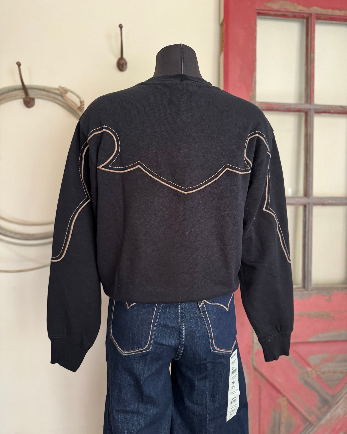 Black jacket with white stitching on a mannequin against a red and white wall.