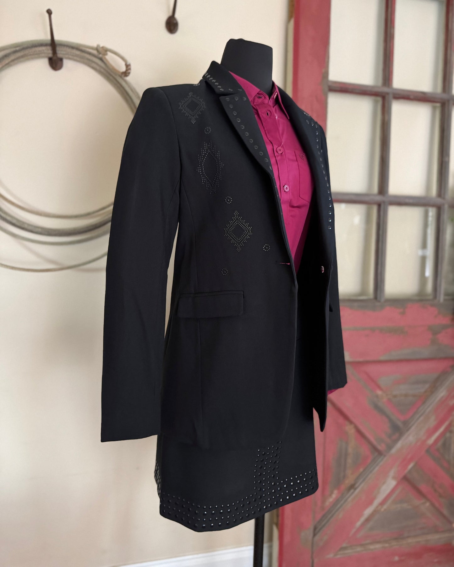 Black coat with pink shirt on a mannequin against a neutral wall.