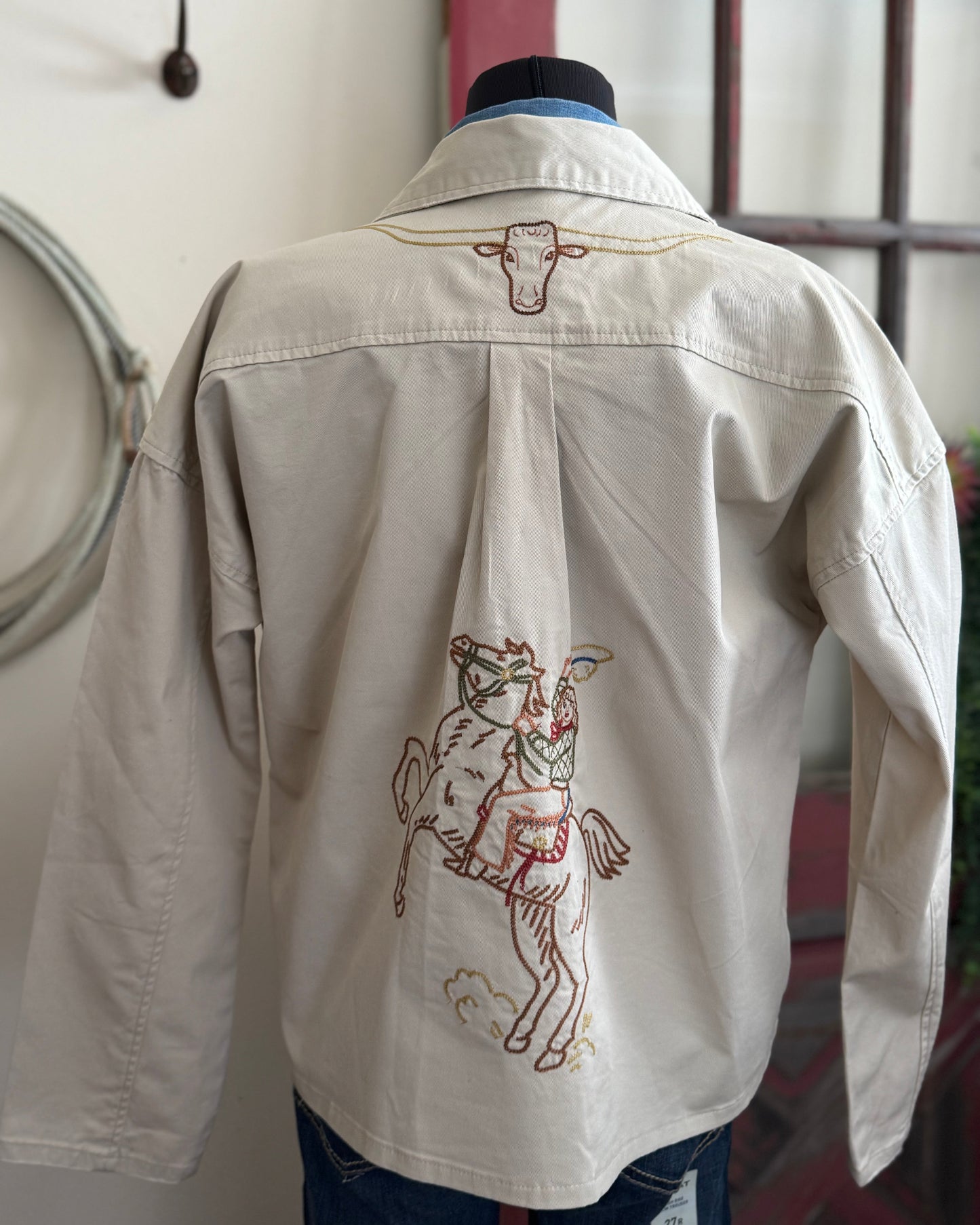 White shirt with embroidered designs on a mannequin against a neutral background