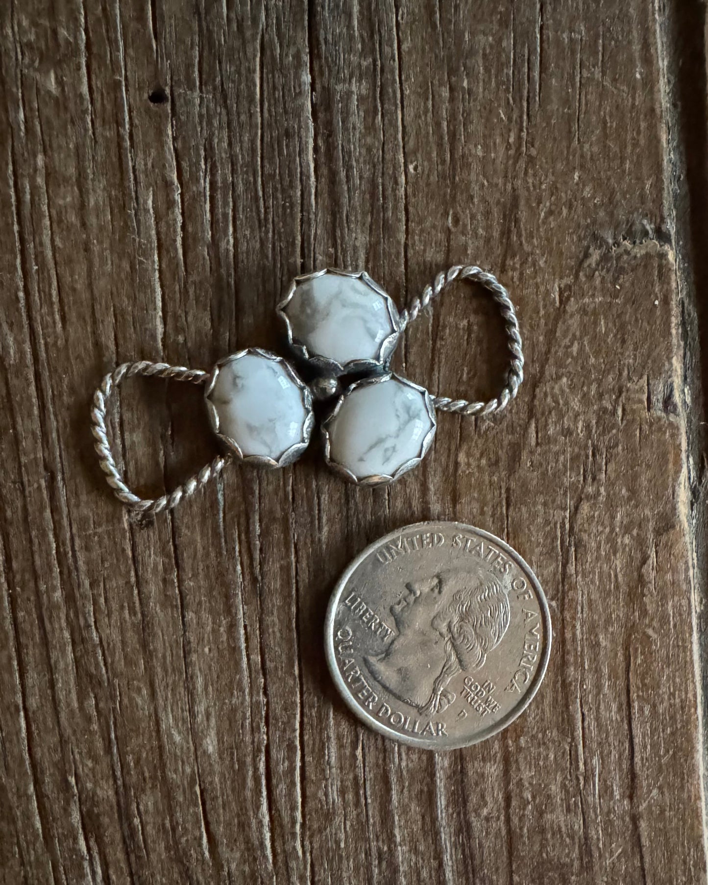 Silver twilly slide with white stones next to a U.S. quarter on a wooden surface