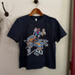 Navy blue t-shirt with graphic design on a wooden hanger against a white wall.