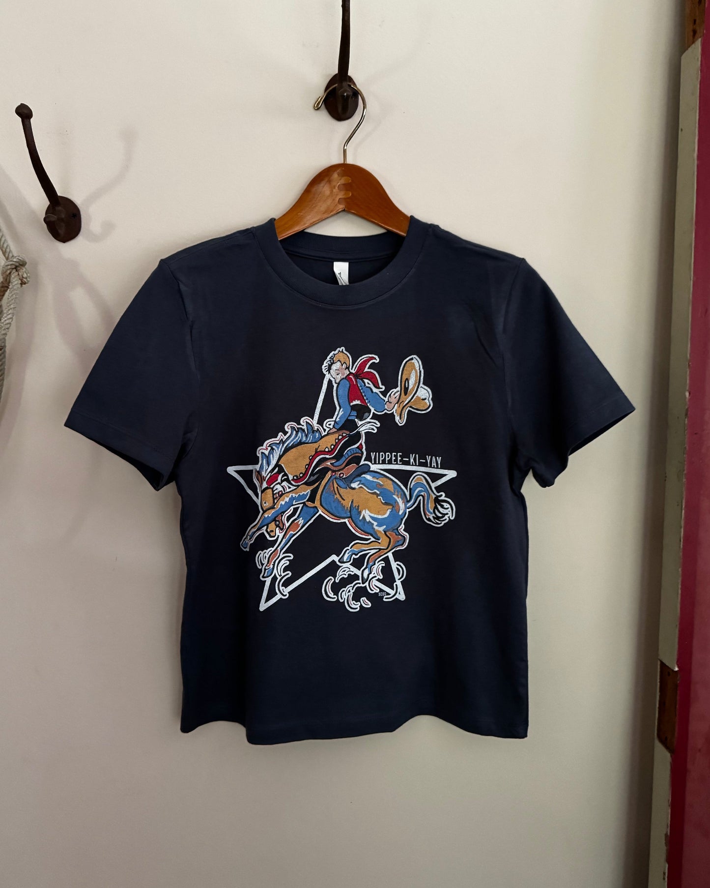 Navy blue t-shirt with graphic design on a wooden hanger against a white wall.