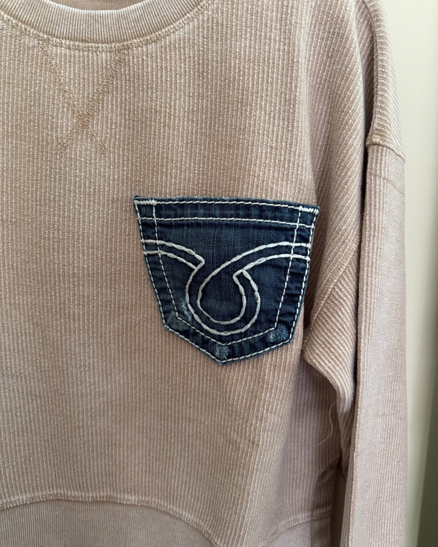 Close-up of a beige corduroy shirt with a brand logo on the pocket.