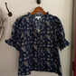 Navy floral blouse hanging on a wooden hanger against a white wall.