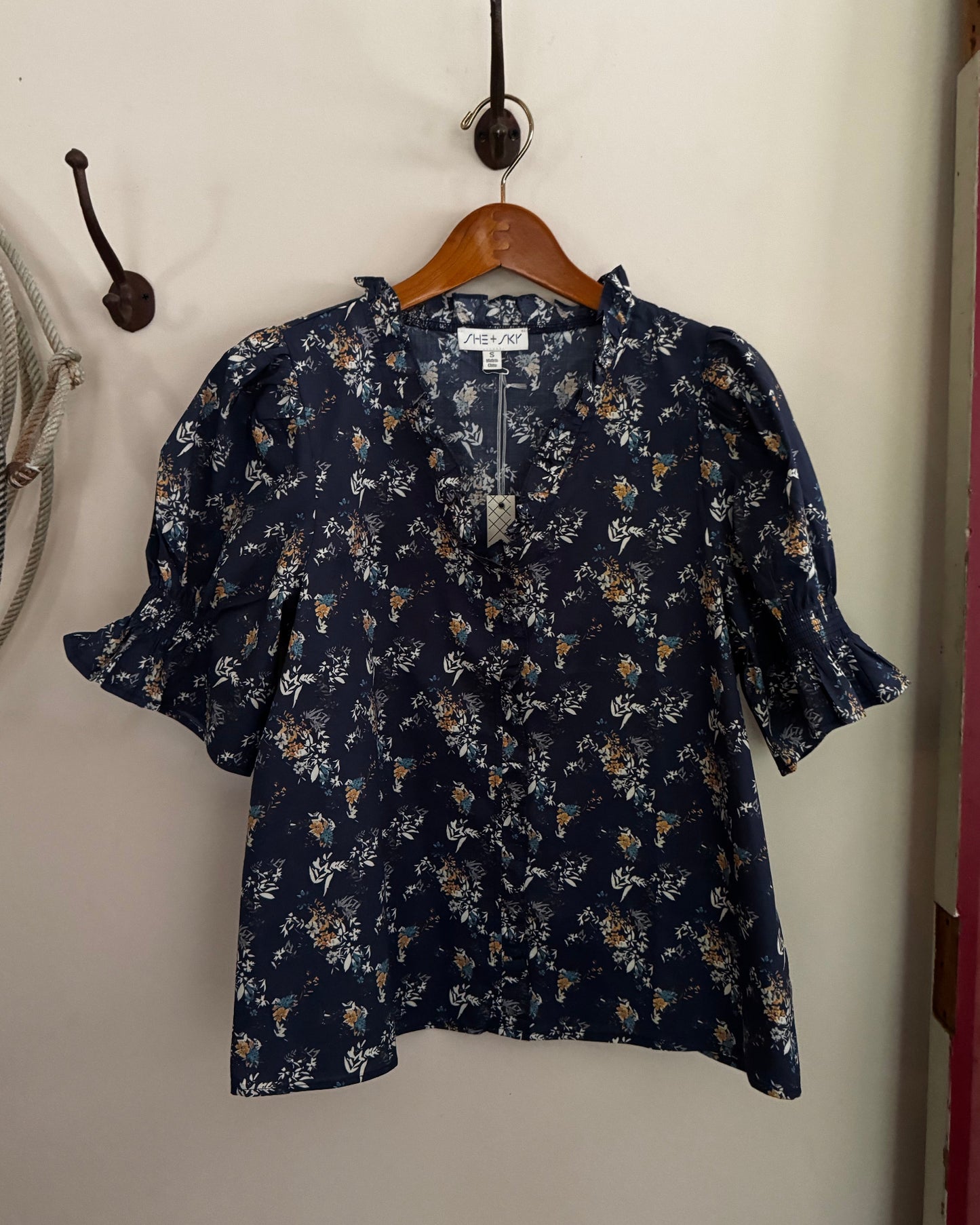 Navy floral blouse hanging on a wooden hanger against a white wall.