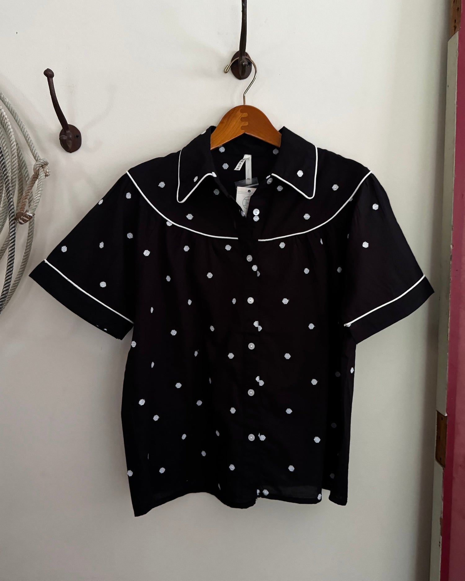 Black shirt with white polka dots on a hanger against a white wall.