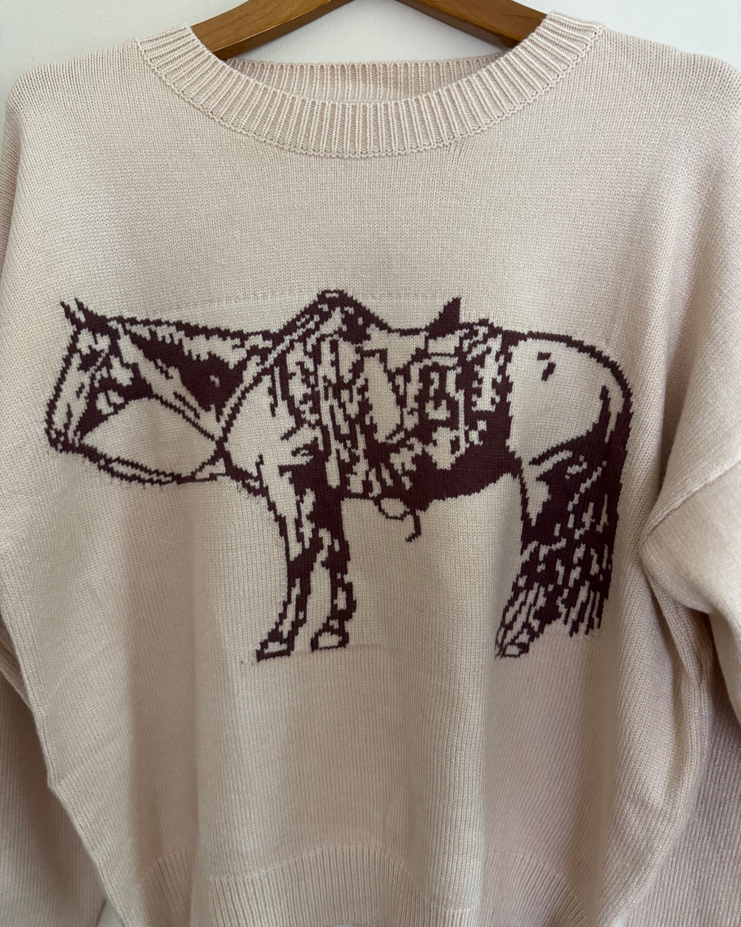 Beige sweater with a horse design on a hanger