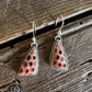 A pair of silver dangle earrings with triangular coral inlay, displayed on a rustic wooden surface.