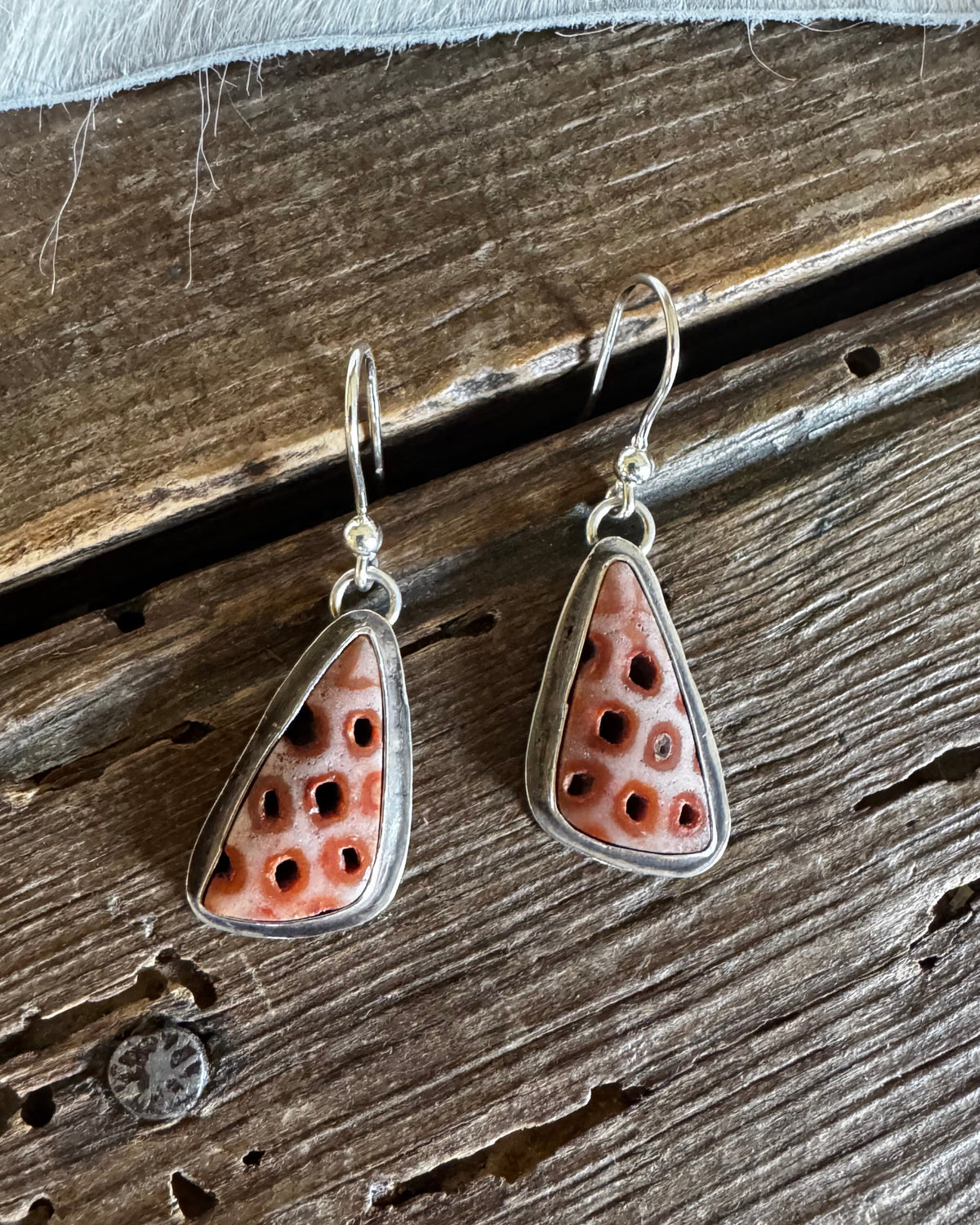 A pair of silver dangle earrings with triangular coral inlay, displayed on a rustic wooden surface.