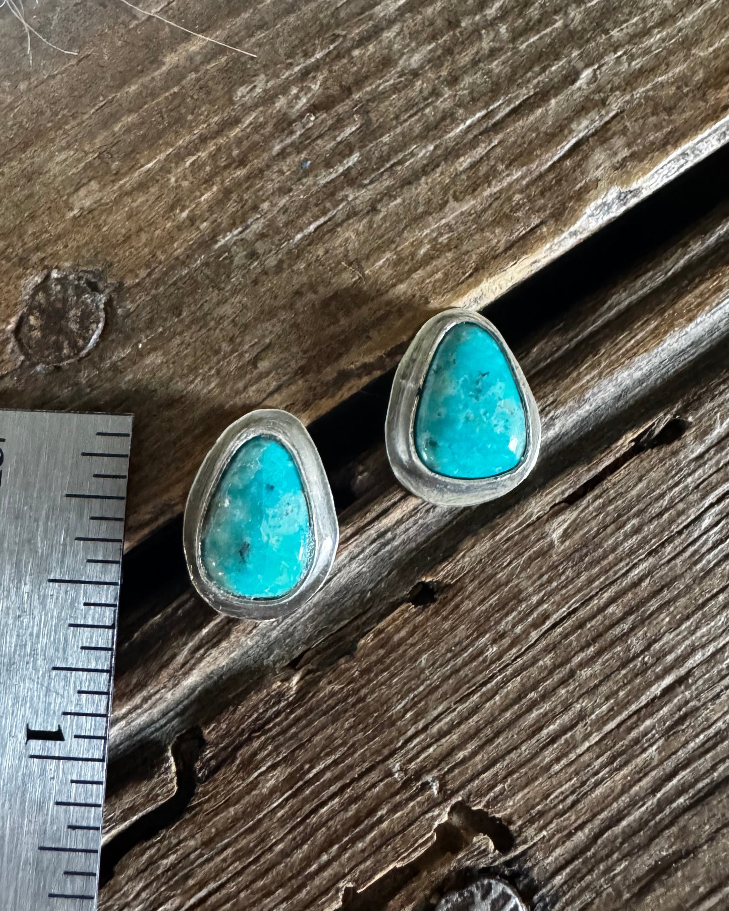 Turquoise stud earrings on a wooden surface with a ruler for scale.