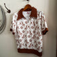 White shirt with brown collar and cuffs hanging on a wooden hanger against a white wall.