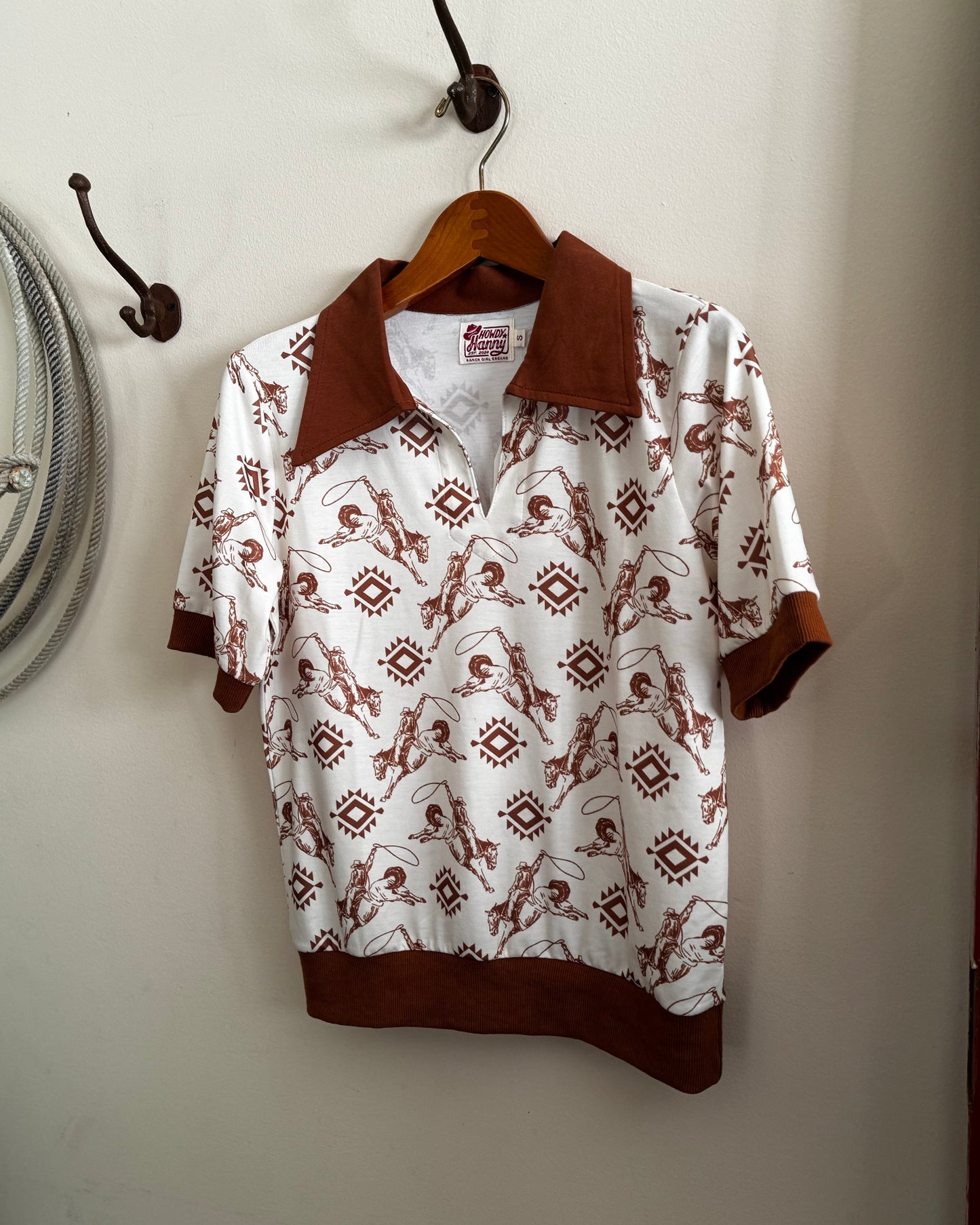 White shirt with brown collar and cuffs hanging on a wooden hanger against a white wall.